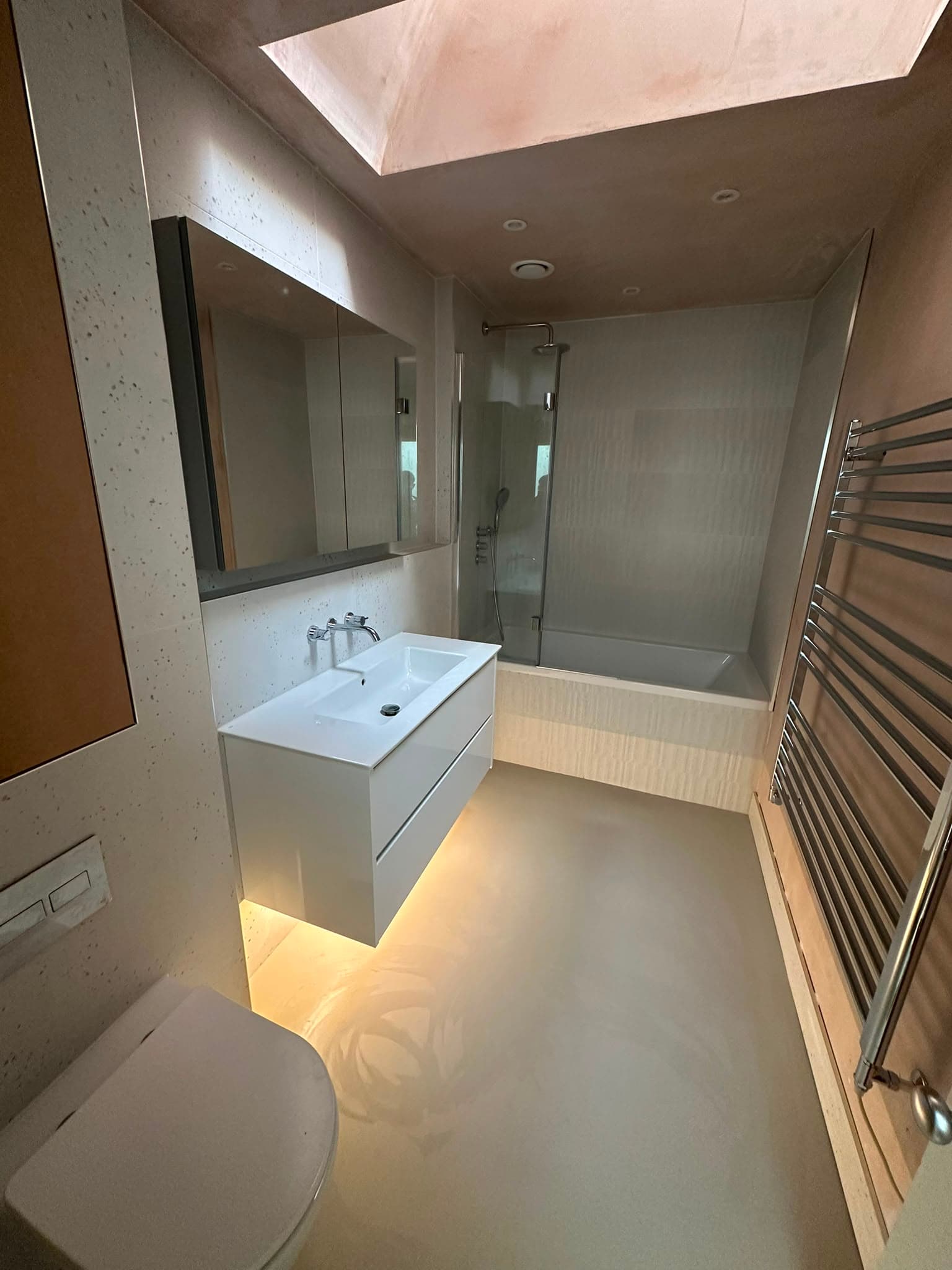 Full bathroom with floating vanity, under-unit LED lighting, bath with shower screen and chrome towel rail