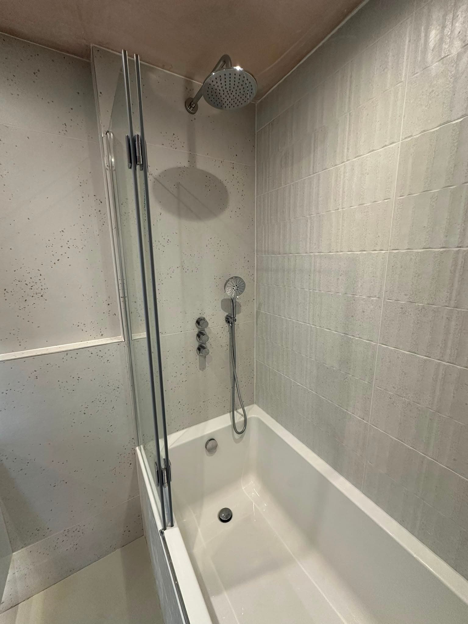 Walk-in shower with rain head and hand shower over bath, bifold glass screen and large format tiles