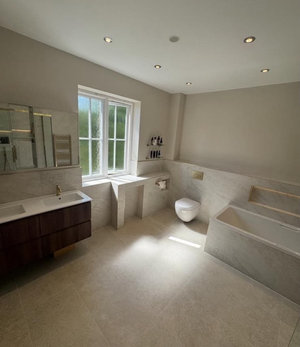Spacious luxury bathroom with large cream stone tiles, wall-hung WC and designer bath surround