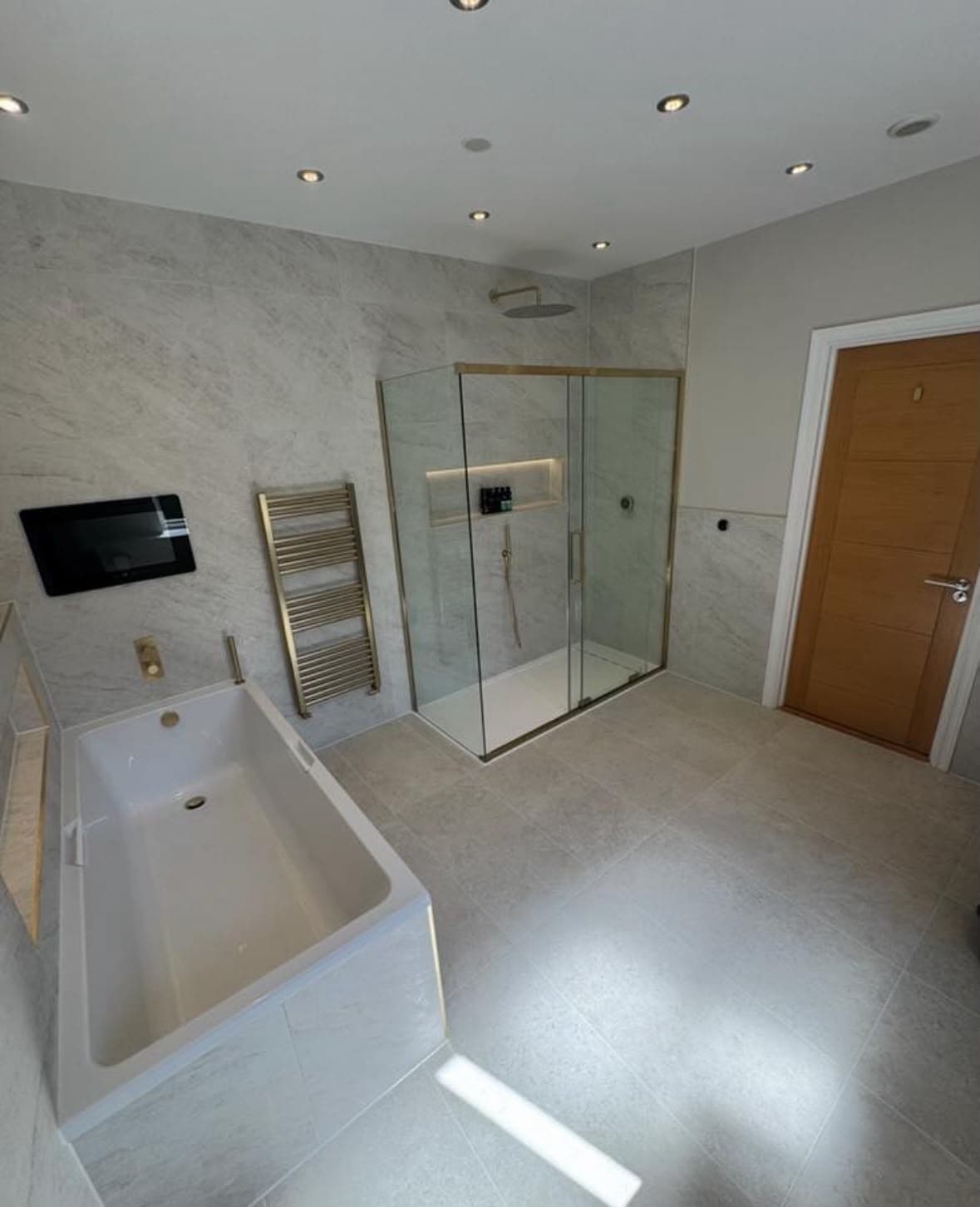 Spacious marble bathroom with freestanding bath, brass-framed glass shower enclosure and smart TV