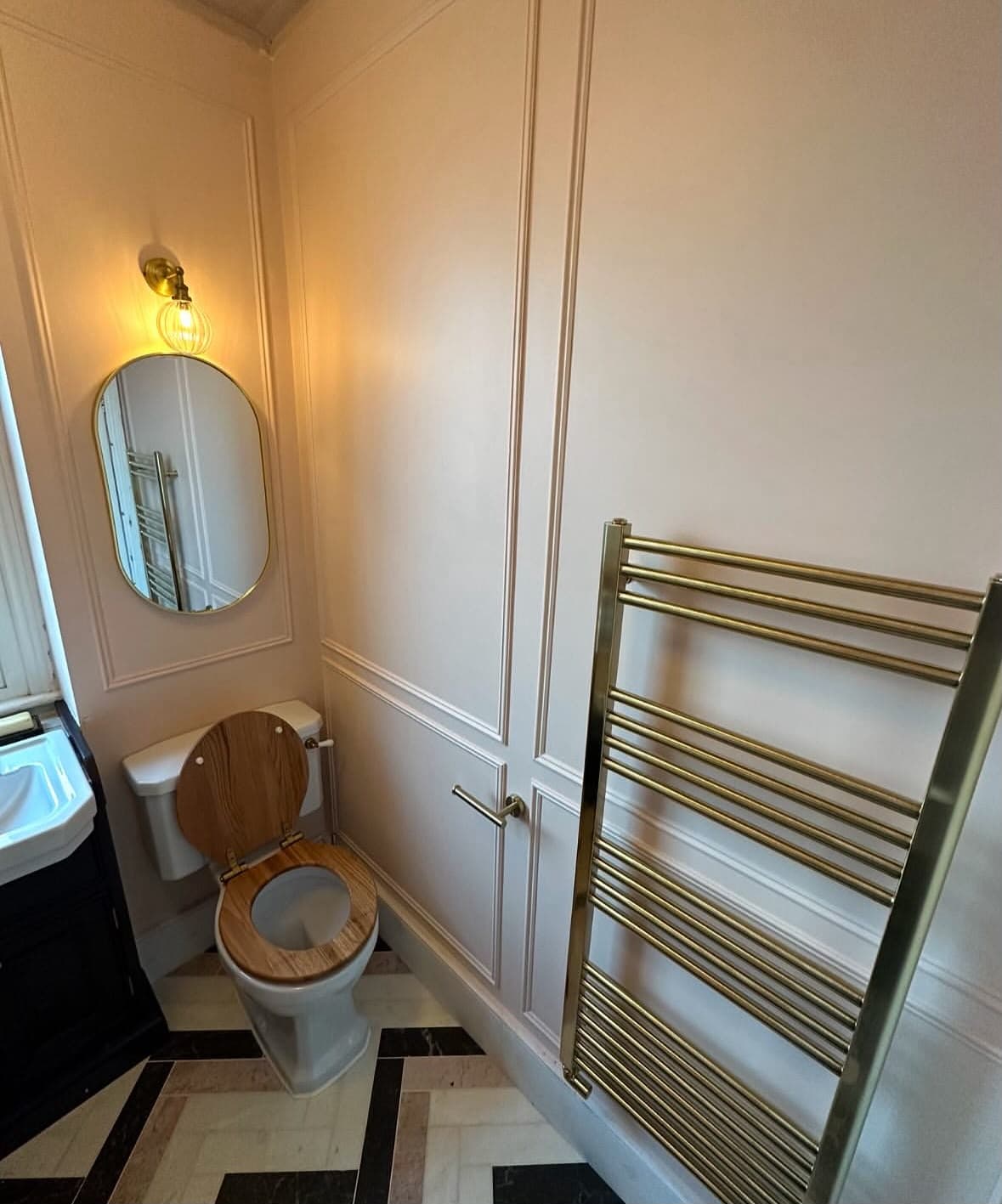 Victorian cloakroom with wall panelling, brass oval mirror, gold heated towel rail and chevron marble floor