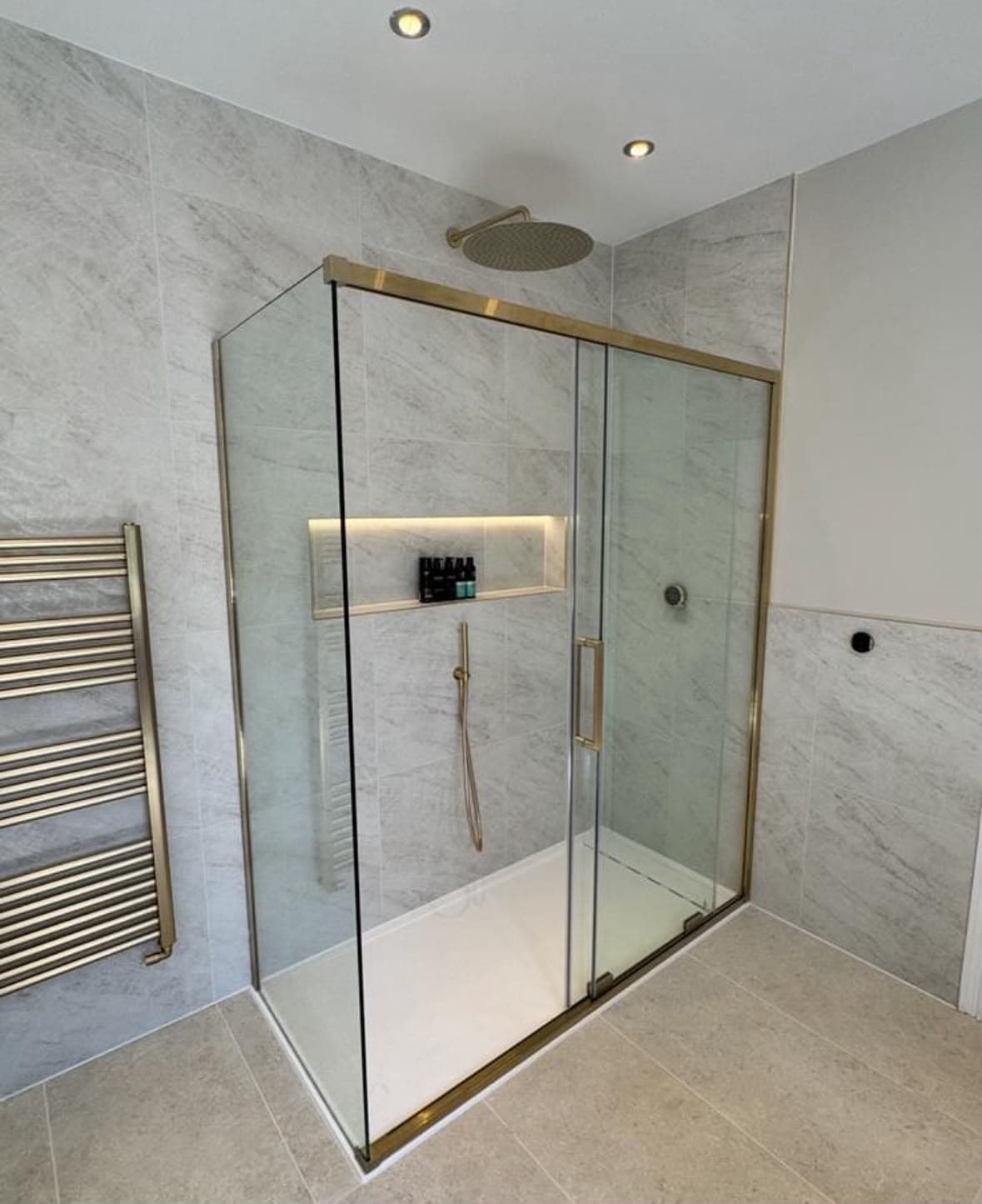 Marble shower enclosure with brass frame, overhead rain shower and illuminated niche shelf